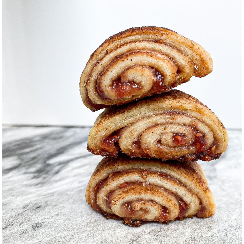 Raspberry Rugelach, flakey pastry swirled with raspberry filling, three pieces stacked and coated with cinnamon sugar.